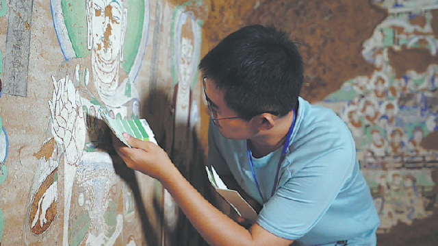 Хань Маоюань держит цветовую диаграмму, чтобы определить оттенки цветов на фреске в пещере Ах-Ай в Синьцзян-Уйгурском автономном районе.